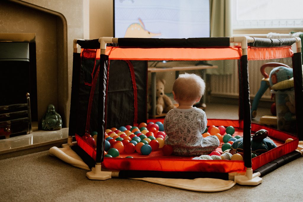 Bébé assis dans un parc bébé hexagonal rempli de balles, posé au sol dans un salon