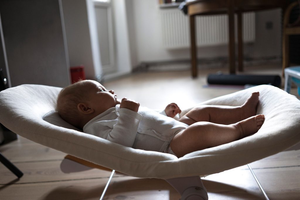Bébé éveillé allongé dans un transat en tissu posé au sol du salon