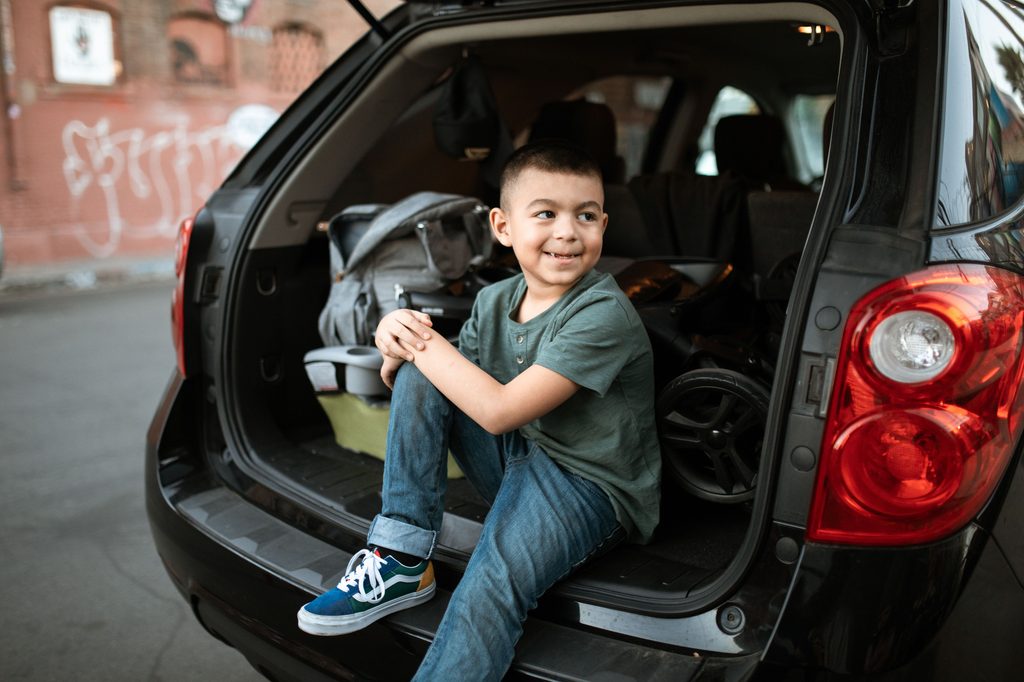 Enfant assis dans le coffre d'une voiture chargée de bagages avant un départ en week-end