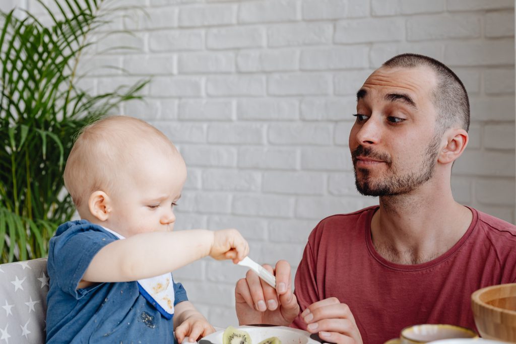 Papa qui regarde son bébé manger seul à table